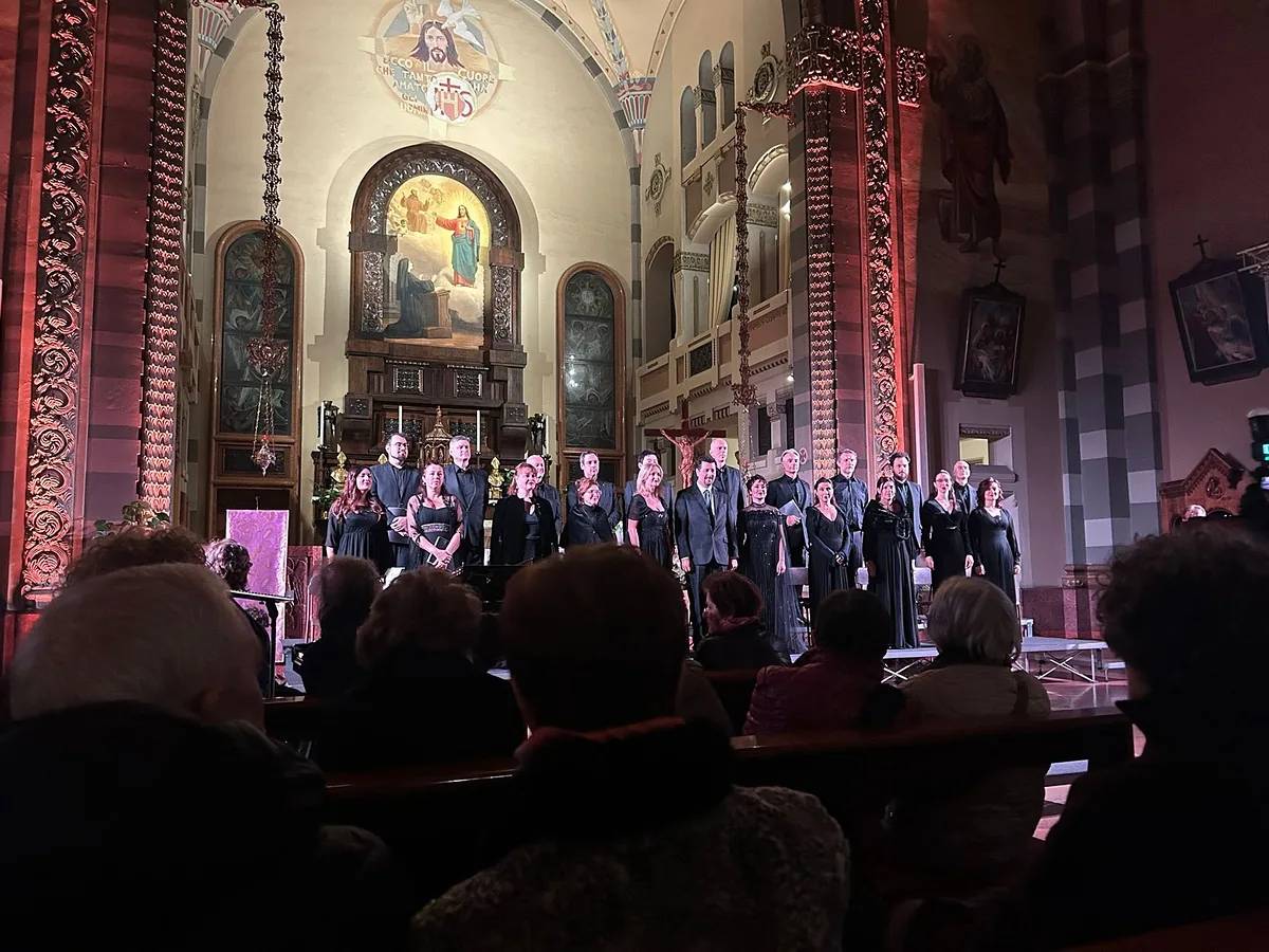 Il Coro Filarmonico G.B. Pergolesi schierato davanti all'altare di una chiesa illuminata, con il pubblico in primo piano